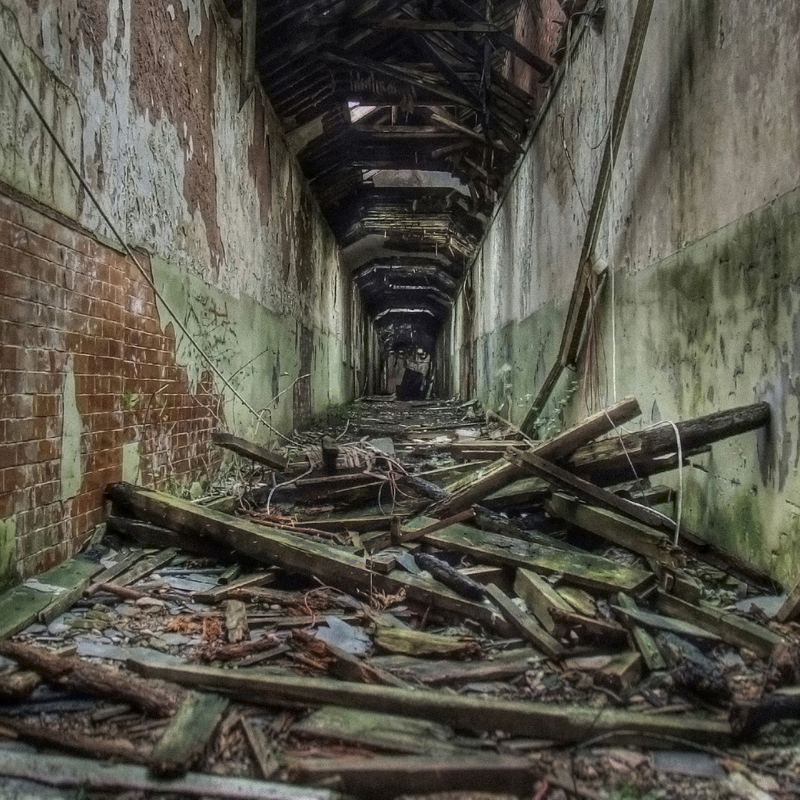 Forgotten asylum hallway in ruins, paint peeling from the walls and ceiling